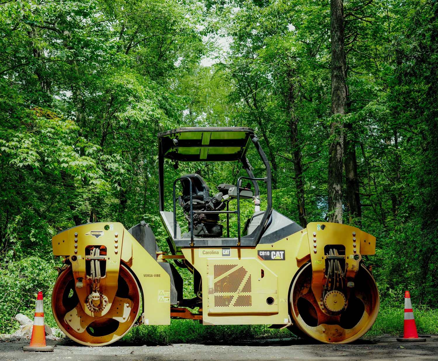A tandem asphalt roller parked at the edge of green woods