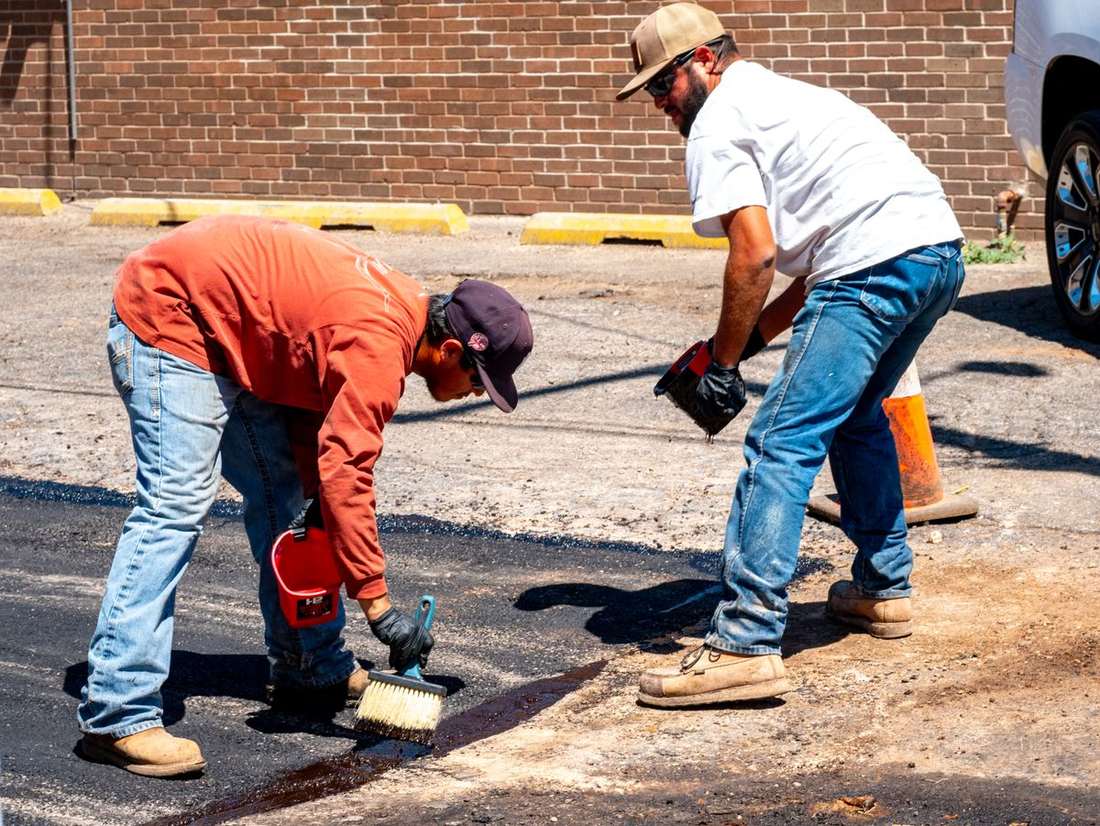 Two workers patching a section of asphalt